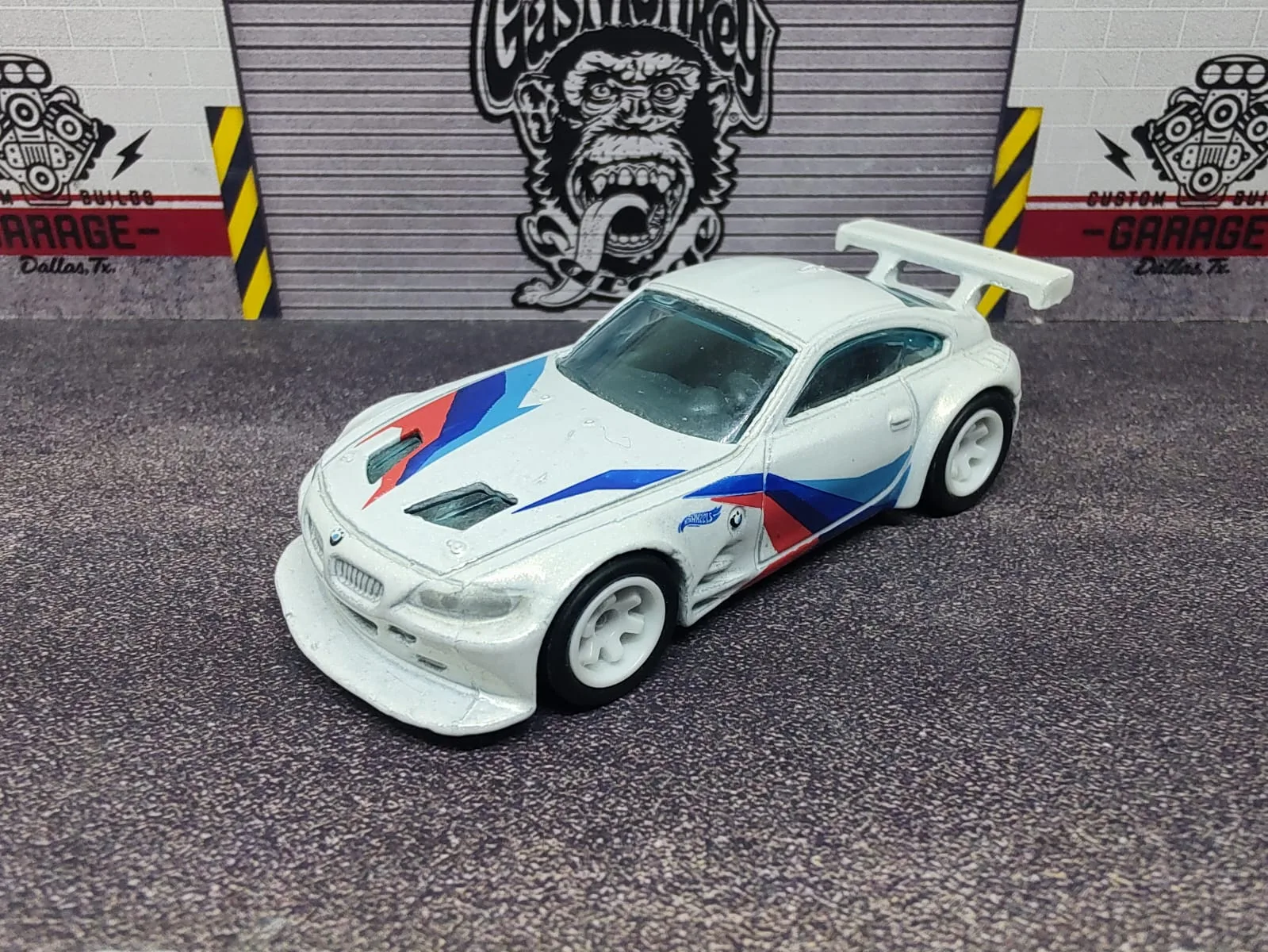 BMW Z4 M Motorsport — blanco con franjas azules y rojas, número 4, alerón blanco y llantas blancas; ejemplar A