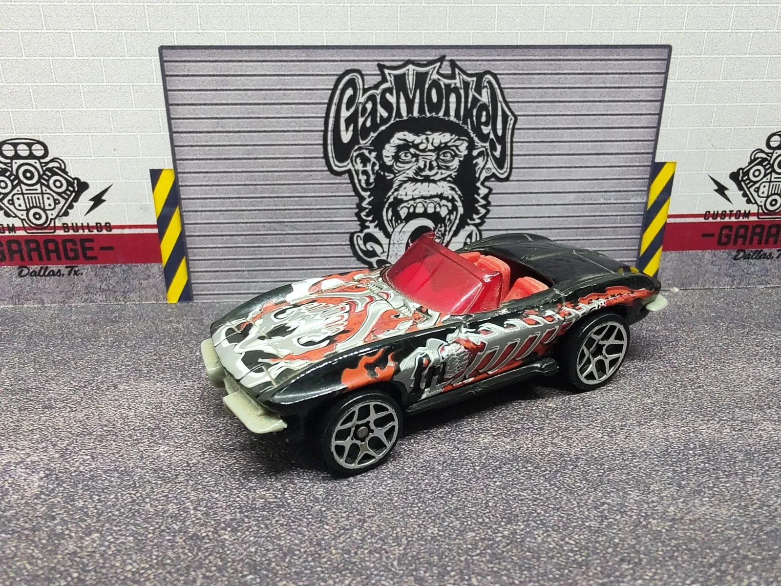 ’65 Corvette — plateado y negro con llamas naranjas, habitáculo rojo y techo abierto