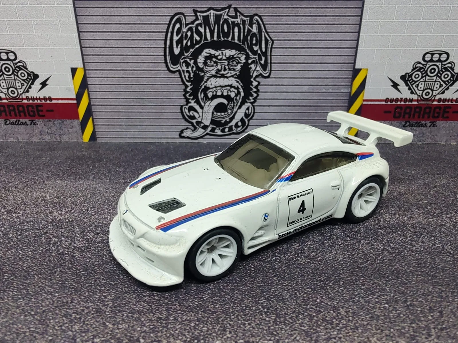 BMW Z4 M Motorsport — blanco con franjas azules y rojas, número 4, alerón blanco y llantas blancas; ejemplar B