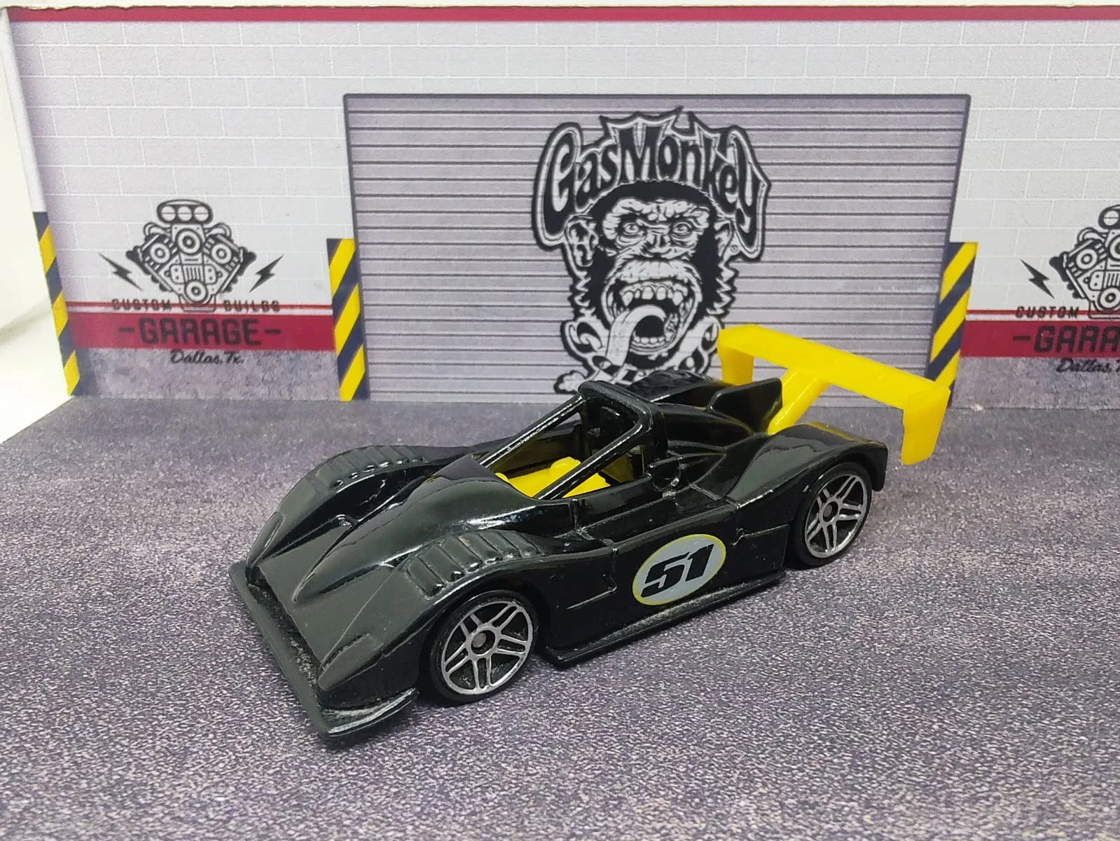 Ferrari 333 SP — gris oscuro con detalles amarillos, alerón amarillo y número decorativo 51