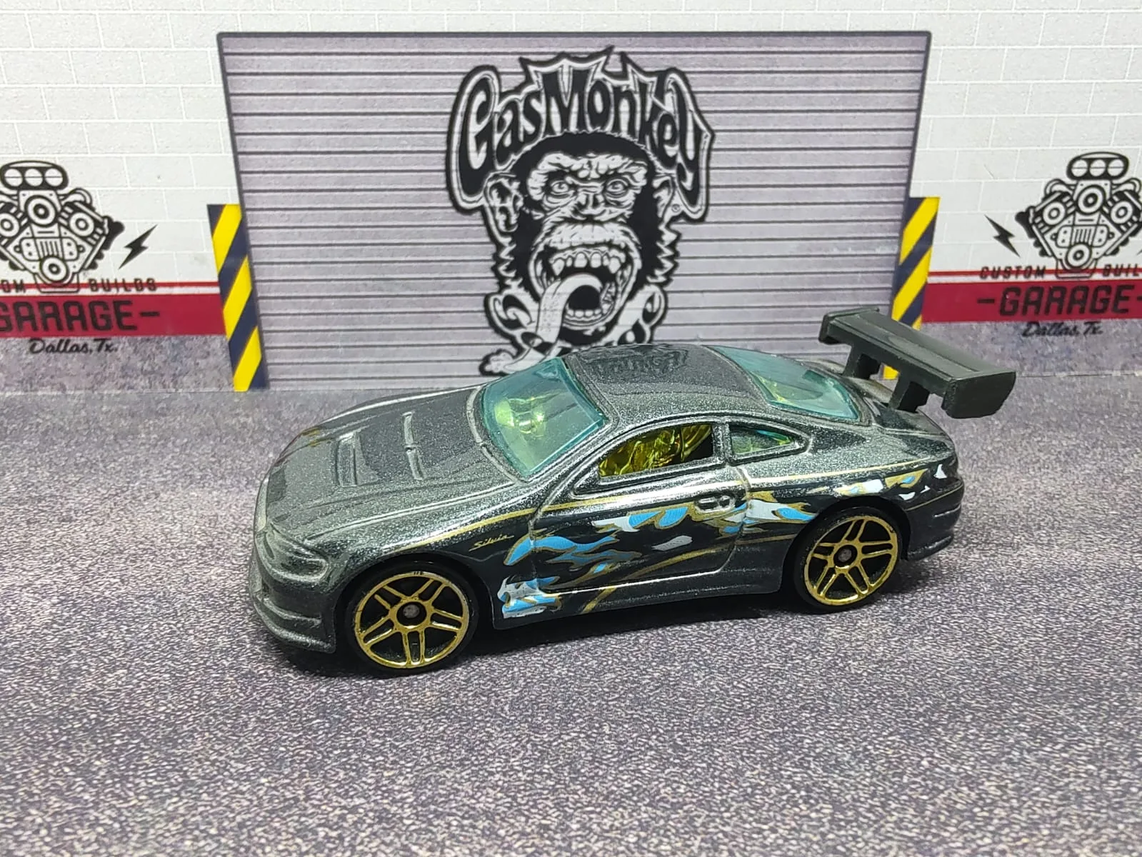 Nissan Silvia S-15 — gris oscuro con decoración azul, alerón negro y llantas doradas