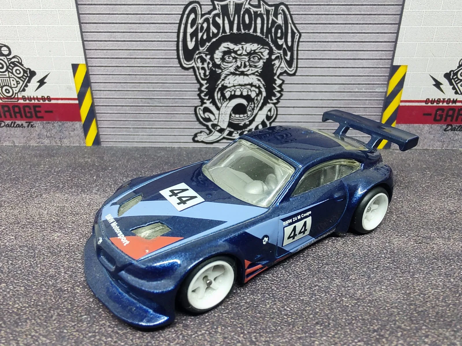 BMW Z4 M Motorsport — azul oscuro con gráficos blancos, negros y naranjas, número 44 y llantas blancas