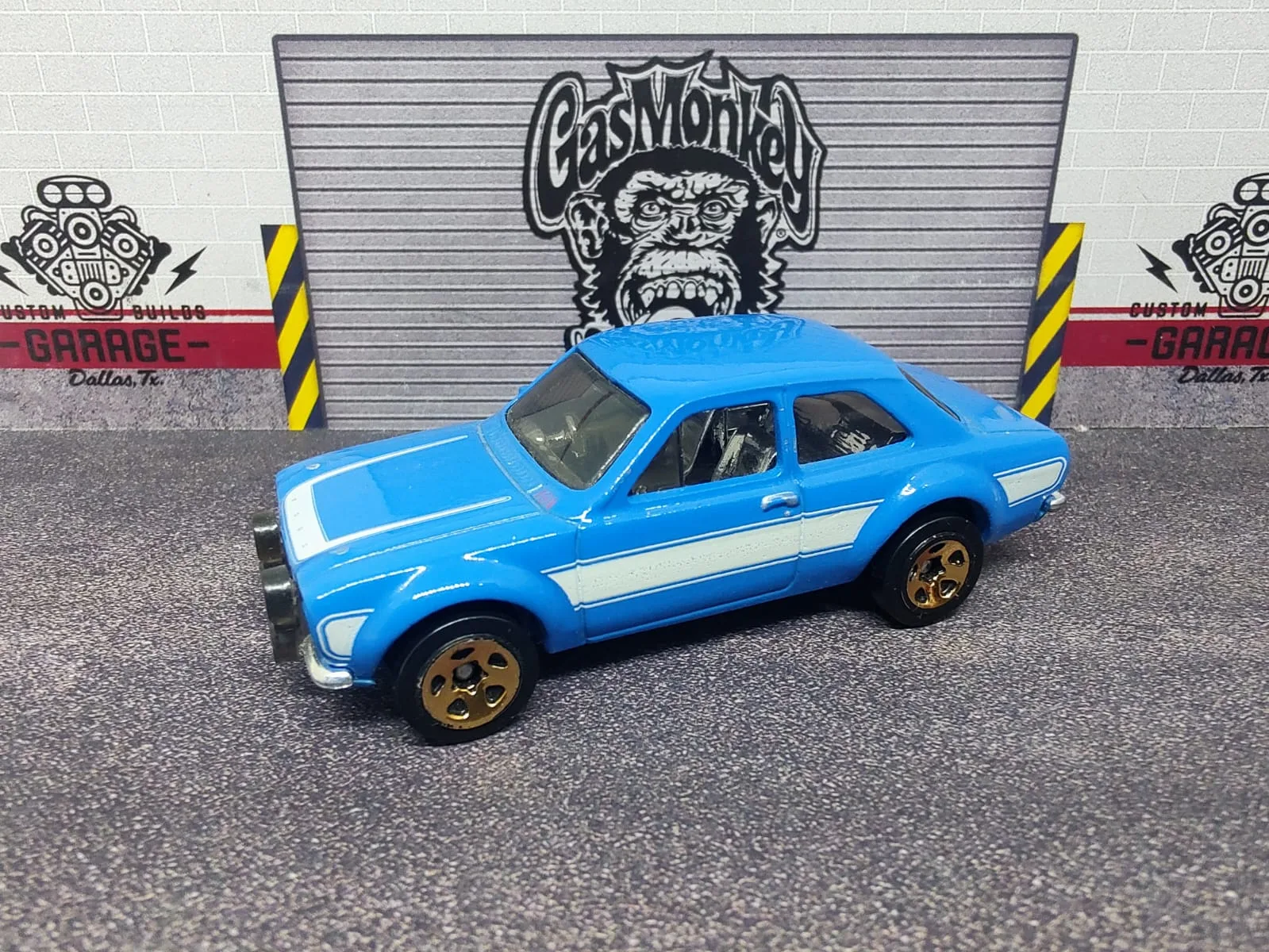 ’70 Ford Escort RS1600 — azul con franjas blancas, ruedas doradas