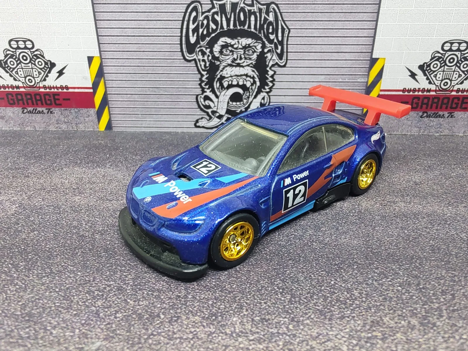 BMW M3 GT2 — azul con decoración M Power, número 12, alerón naranja y llantas doradas