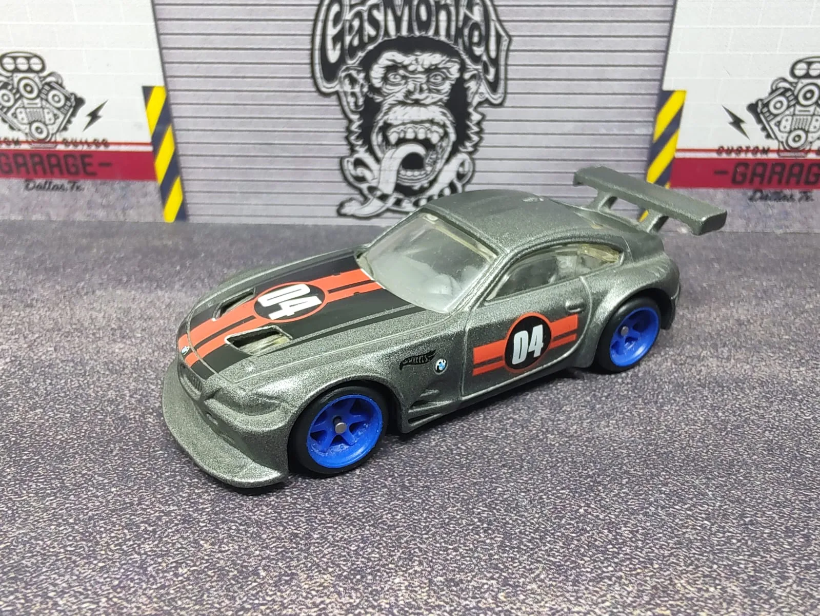 BMW Z4 M Motorsport — gris metalizado con franjas negras y naranjas, número 04, alerón gris y llantas azules