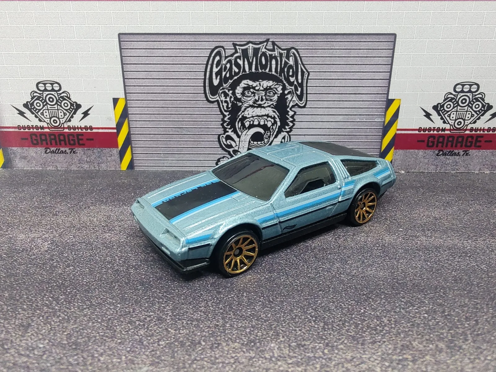 ’81 DeLorean DMC-12 — azul claro metalizado con franjas negras y llantas doradas