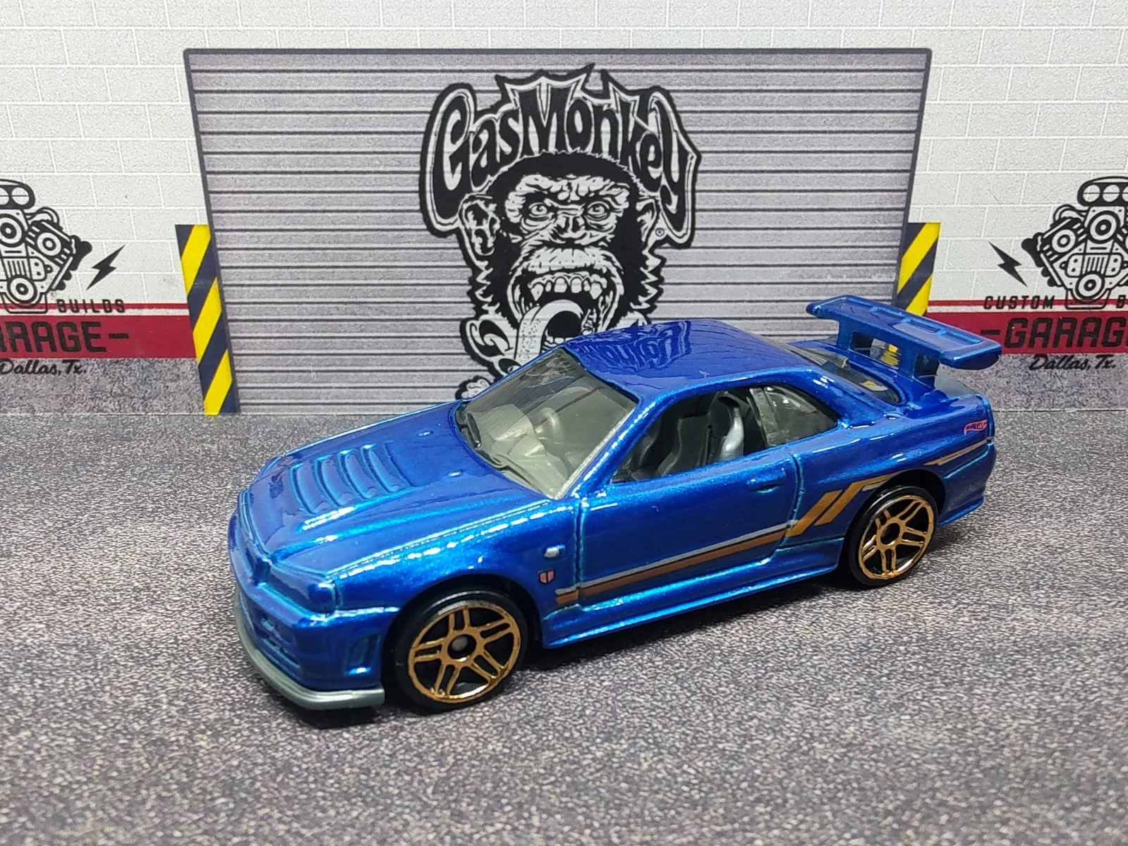 Nissan Skyline GT-R (R34) — azul metalizado con franjas laterales doradas, alerón y llantas doradas