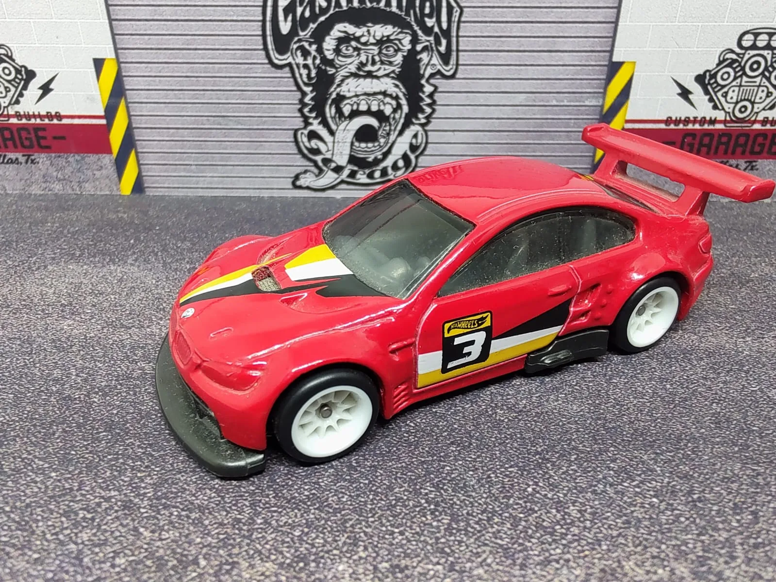 BMW M3 GT2 — rojo con gráficos negros y amarillos, número 3, alerón rojo y llantas blancas