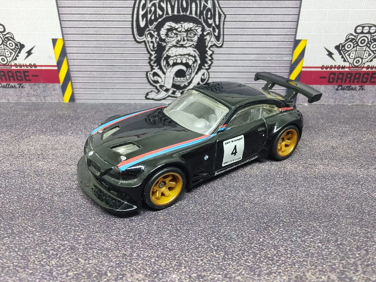 BMW Z4 M Motorsport — negro con franjas azules y rojas, número 4, alerón negro y llantas doradas