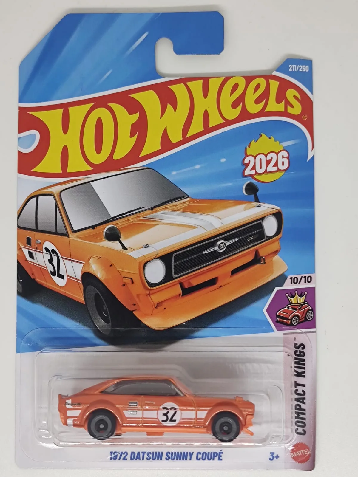 1972 Datsun Sunny Coupé — naranja con franjas blancas y número 32; en blíster