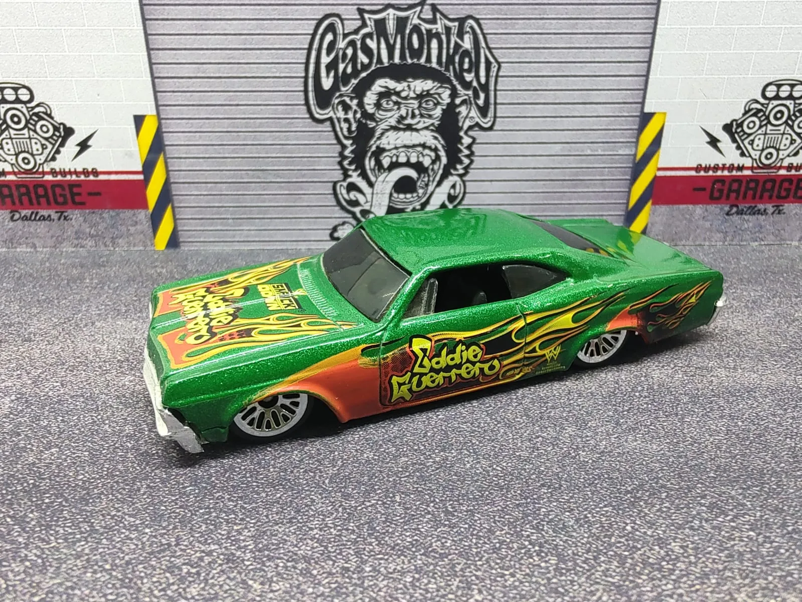 ’65 Chevy Impala — verde metalizado con llamas amarillas, detalles naranjas y gráfica Eddie Guerrero
