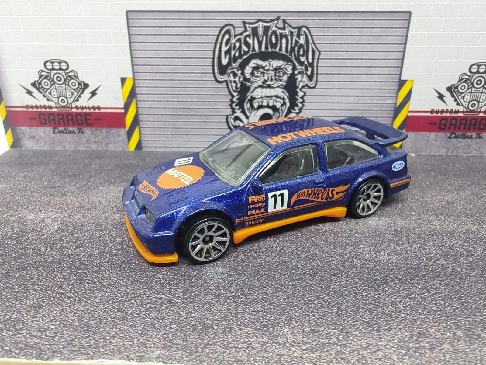 ’87 Ford Sierra Cosworth — azul con gráficas naranjas de Hot Wheels Racing, marcas de rally y número decorativo 11