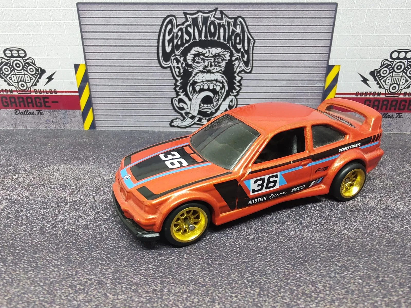 BMW E36 M3 Race — naranja con franjas negras, número 36 y llantas doradas