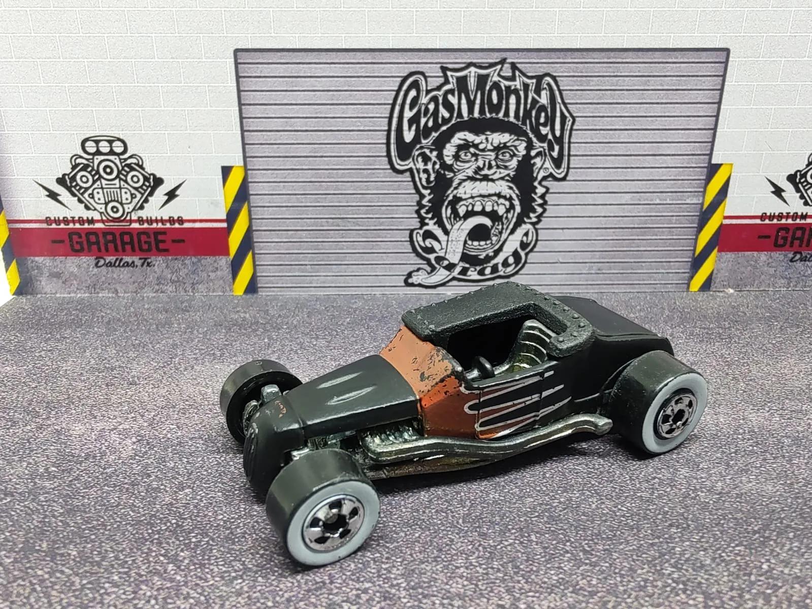 Track T — hot rod negro de habitáculo abierto con detalles marrones y motor y escapes plateados